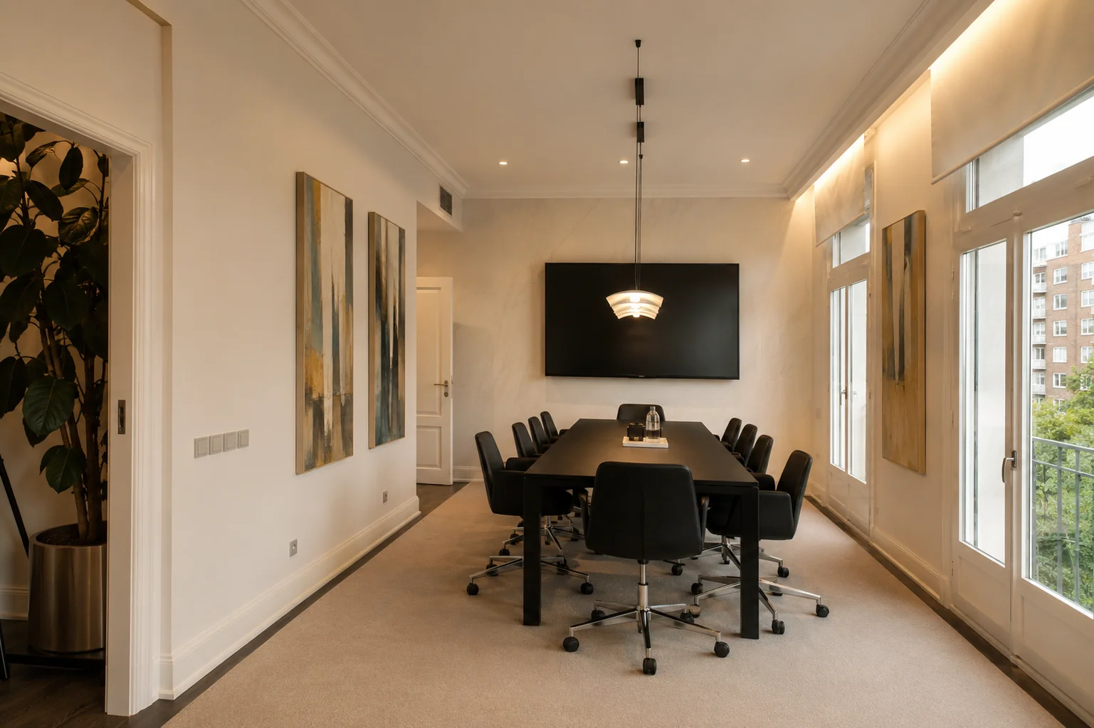 Sala de reuniones moderna con una mesa larga y sillas negras, decorada con pinturas abstractas y una pantalla grande en la pared.
